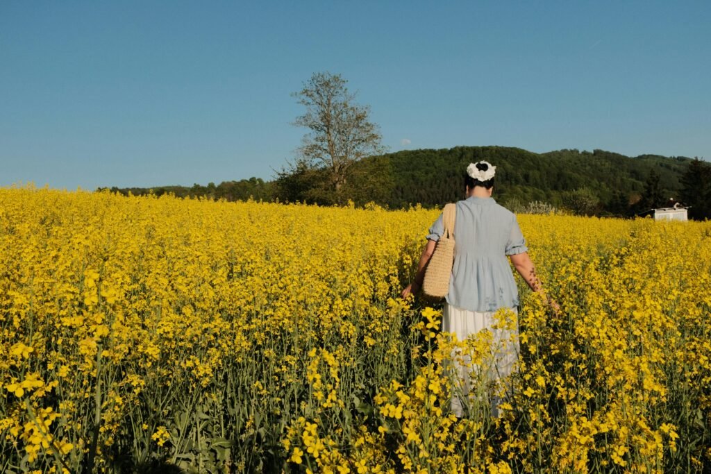 A serene scene of a woman in a hat walking through a vibrant yellow rapeseed field.